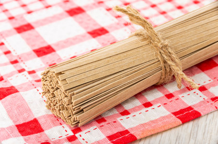 Bunch of buckwheat noodles on checkered napkin on wooden table