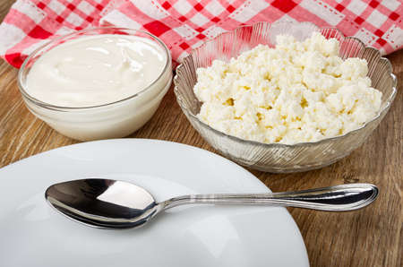 Checkered napkin, transparent glass bowls with sour cream and cottage cheese, spoon in white plate...