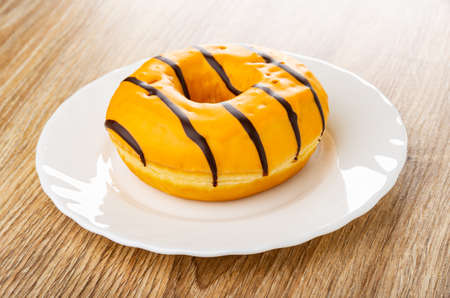 Yellow donut with chocolate stripes in white plate on wooden tableの写真素材