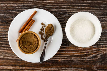 Cinnamon sticks, bamboo bowl with ground cinnamon, spoon with cinnamon in white plate, bowl with sugar on wooden table. Top viewの写真素材
