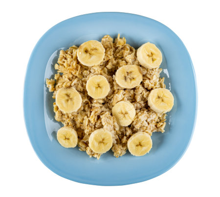 Oatmeal dairy porridge with slices of banana in light-blue plate isolated on white background. Top viewの写真素材