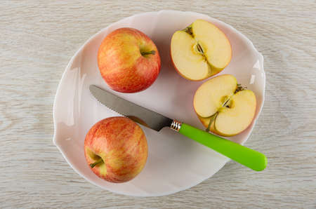 Ripe red apples, halves of apple, table knife in white glass dish on wooden table. Top viewの写真素材