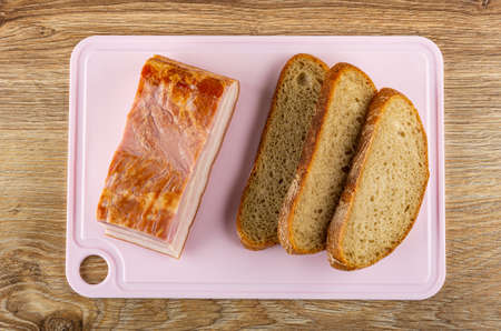 Piece of smoked brisket, slices of bread on pink cutting board on wooden table. Top viewの写真素材