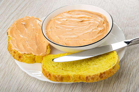 White glass bowl with creamy fish oil, sandwich, slices of cornbread, table knife in plate on wooden tableの写真素材