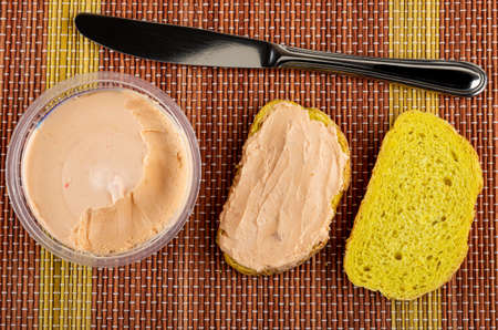 Table knife, plastic jar with creamy fish oil, sandwich, slice of cornbread on bamboo mat. Top viewの写真素材