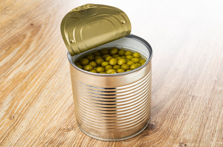 Opened metallic jar with canned green peas on brown wooden tableの写真素材
