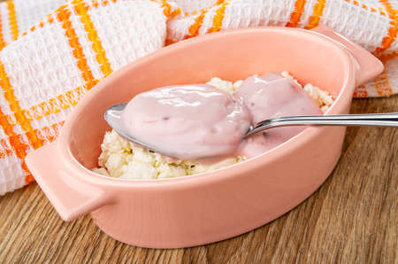 Checkered napkin, spoon of fruit yogurt in pink oval bowl with cottage cheese on wooden tableの写真素材