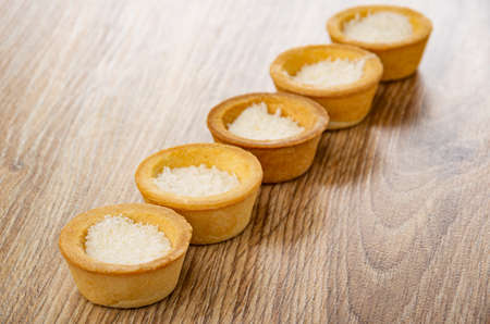 Row of cookies tartlets with coconut shavings on brown wooden tableの写真素材