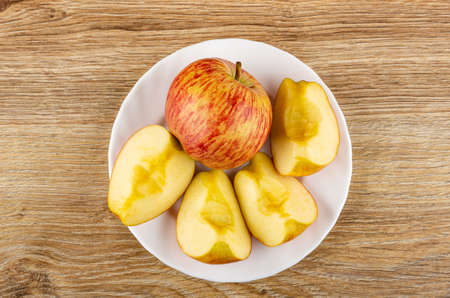 Red striped apple, slices of apple in white plate on wooden table. Top view