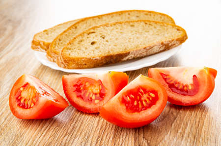 Slices of rye bread in white plate, slices of red tomato on wooden tableの写真素材
