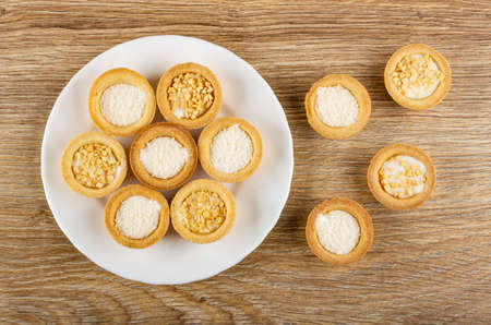 Cookies tartlets with peanut and coconut shavings in white plate, cookies on brown wooden table. Top...