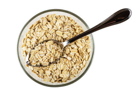 Metallic spoon in transparent bowl with raw oat flakes isolated on white background. Top viewの写真素材
