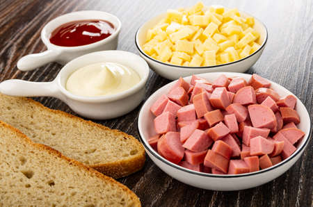 Sauce boats with ketchup and mayonnaise, bowls with small pieces of cheese and sausage, slices of...