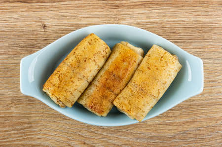 Pancake rolls with filling in light-blue oval bowl on brown wooden table. Top viewの写真素材