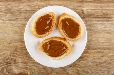 Three sandwiches from wheat bread with boiled sweet condensed milk in white plate on wooden table. Top viewの写真素材