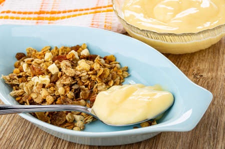 Checkered napkin, transparent bowl with fruit yogurt, muesli with apple and raisin, spoon with...