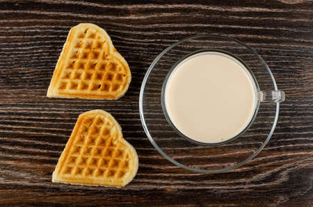 Two heart shape biscuits, cup with fermented baked milk on saucer on dark wooden table. Top viewの写真素材