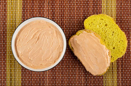 White glass bowl with creamy fish oil, sandwich, slice of cornbread on bamboo mat. Top view