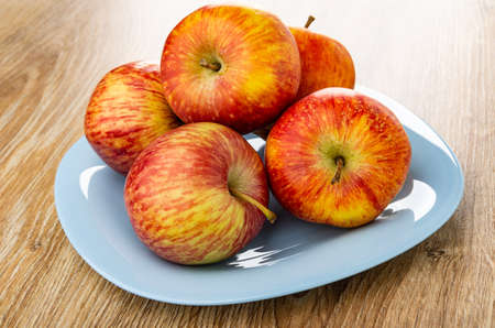 Red striped apples in light-blue plate on brown wooden table