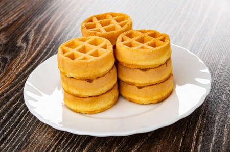 Three stacks of soft biscuit waffles round shape in white plate on dark wooden tableの写真素材