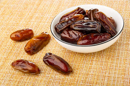 Few dates on brown mat, dried date fruit in white glass bowl