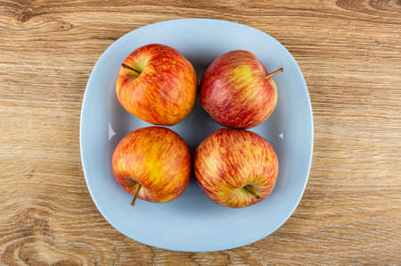 Red striped apples in light-blue plate on brown wooden table. Top view