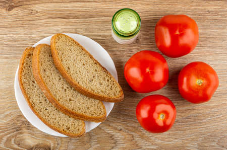 Slices of rye bread in white plate, salt shaker, ripe red tomatoes on wooden table. Top viewの写真素材