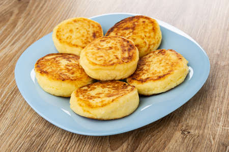 Few cottage cheese pancakes in light-blue plate on brown wooden table