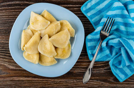 Boiled dumpling with butter in light-blue plate, fork on striped napkin on dark wooden table. Top viewの写真素材