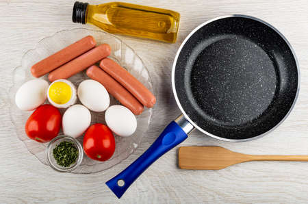 Eggs, red tomatoes, salt shaker, bowl with dried parsley, sausages in transparent plate, bottle of...