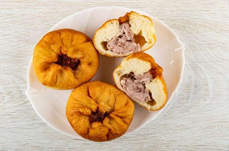 Small fried pies with meat filling (belyash), halves of pie in white dish on wooden table. Top view