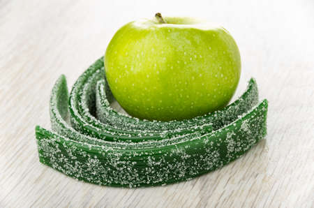 Few twisted thin strips of green marmalades, ripe apple on wooden table