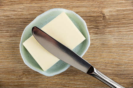 Metallic table knife on small piece of butter in spotted light-blue plate on brown wooden table. Top viewの写真素材