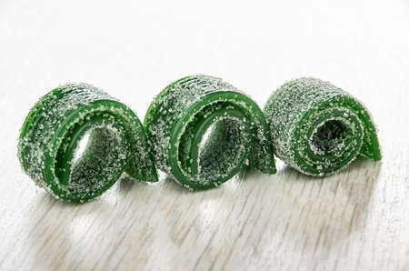 Row of small rolls of thin strips of green marmalades on wooden tableの写真素材