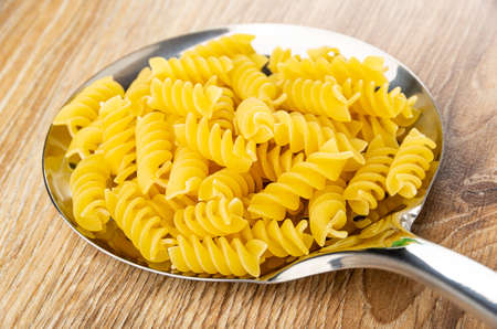 Metallic skimmer with raw pasta fusilli on wooden table