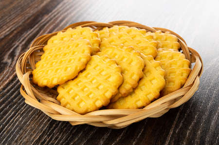 Waffle cookies in wicker basket on dark wooden table
