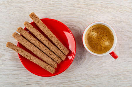 Crusty sticks with cream filling in red saucer, coffee espresso in cup on wooden table. Top view