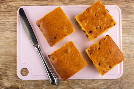 Four biscuit cookies with raisin and table knife on pink cutting board on wooden table. Top view