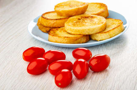 Toasted wheat bread in blue plate, few red tomato cherry on wooden table