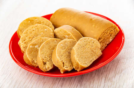 Sweet creamy sausage with peanut (oriental sweets), slices of sweets in red saucer on wooden table
