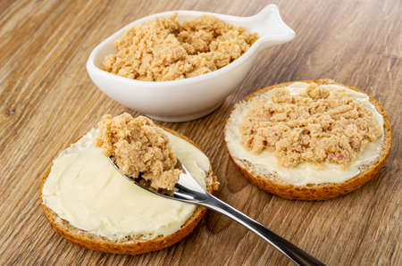 Canned sterilized cod caviar in white bowl in fish shape, teaspoon with cod caviar on sandwich with...