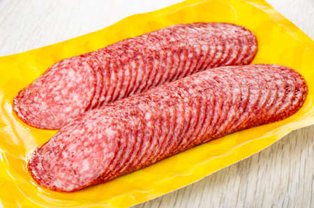 Opened package with slices of sausage salami on wooden tableの写真素材