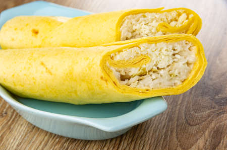 Two tortilla wraps with caesar salad in blue plate on wooden table
