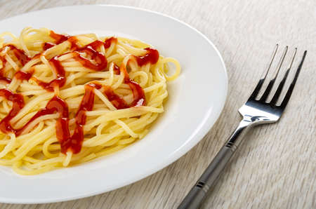 Spaghetti with ketchup in white glass plate, fork on wooden tableの写真素材