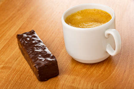Glazed chocolate wafer, white cup with coffee espresso on wooden table
