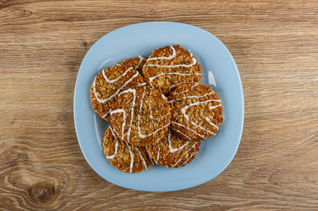 Cookies with white glaze, sunflower seeds and sesame in light-blue plate on wooden table. Top viewの写真素材