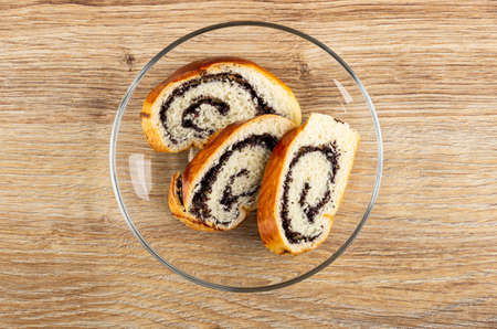 Slices of bun with poppy seed in transparent glass saucer on wooden table. Top viewの写真素材