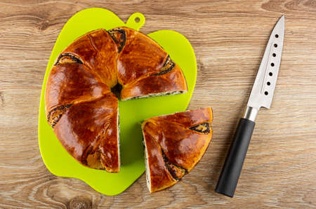 Pieces of bun with poppy seed on green plastic cutting board, kitchen knife on wooden table. Top viewの写真素材