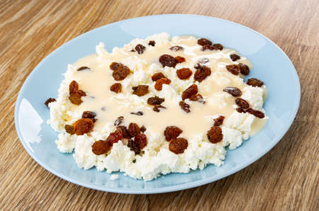 Blue plate of cottage cheese with raisin poured fruit yogurt on wooden tableの写真素材