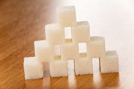 Sugar cubes stacked in pyramid shape on brown wooden tableの写真素材